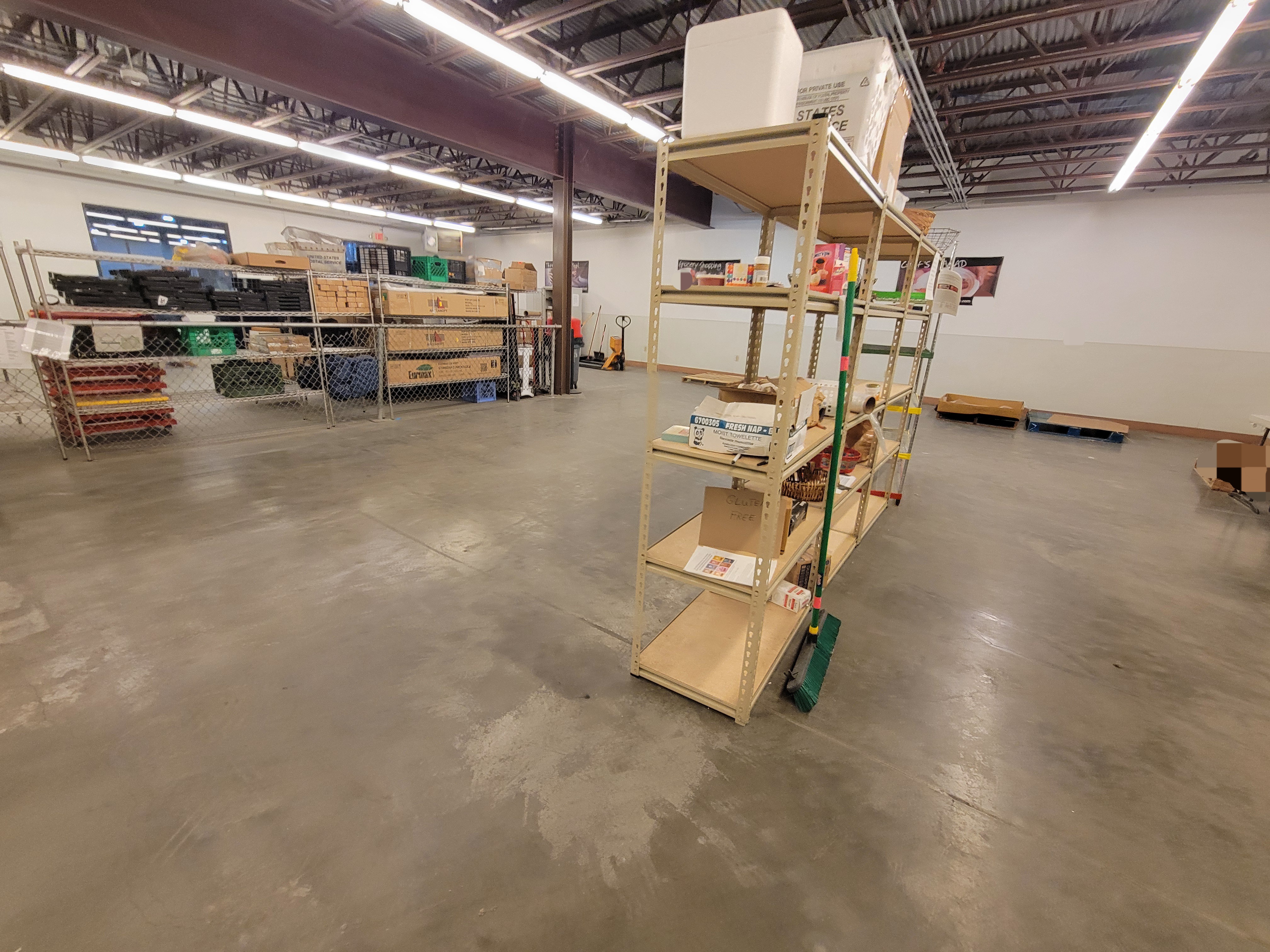 Mostly empty shelves and pallets in a warehouse with gate and more stuff filled shelves behind it.